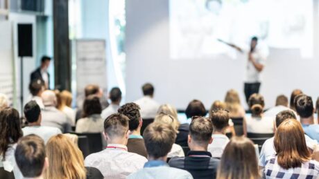 a man speaking in front of a crowd of people in an office setting