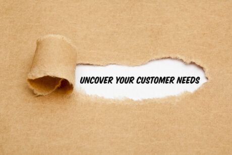 Torn cardboard reveals a white strip with the bold phrase 'UNCOVER YOUR CUSTOMER NEEDS'.