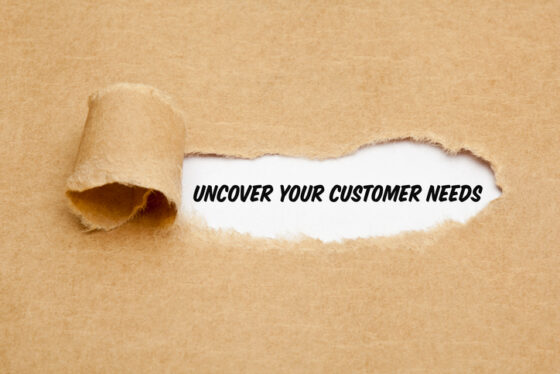 Torn cardboard reveals a white strip with the bold phrase 'UNCOVER YOUR CUSTOMER NEEDS'.