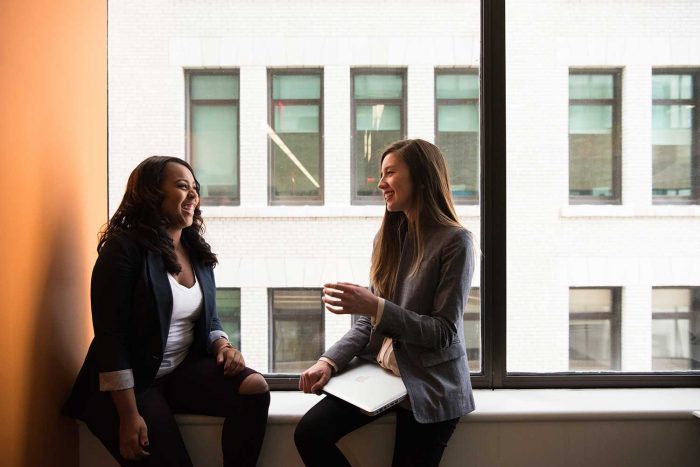 two women talking next to a window