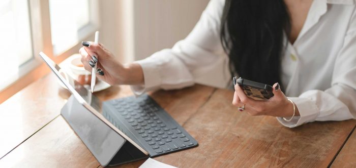 woman working on a tablet with her cell phone in hand