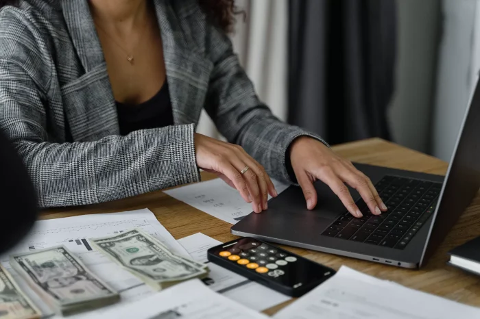 woman-working-on-a-laptop-with-calculator-and-money-next-to-her